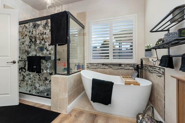 full bath with a stall shower, a freestanding tub, tile walls, and wood finished floors