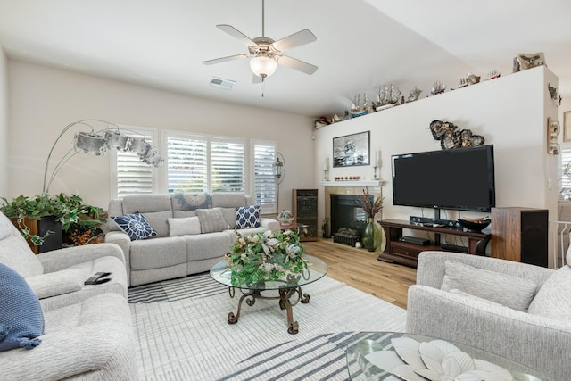 living room with a ceiling fan, visible vents, a fireplace, and wood finished floors