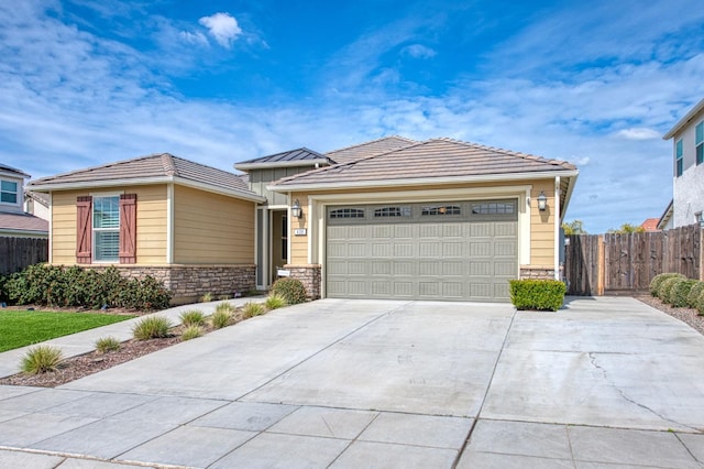 view of front facade featuring stone siding, fence, an attached garage, and concrete driveway