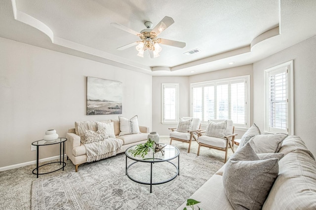 living area featuring a raised ceiling, visible vents, baseboards, and carpet flooring