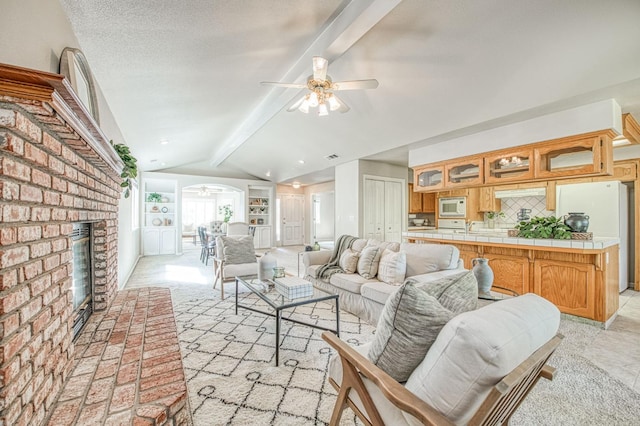 living room featuring built in features, a fireplace, lofted ceiling with beams, ceiling fan, and a textured ceiling