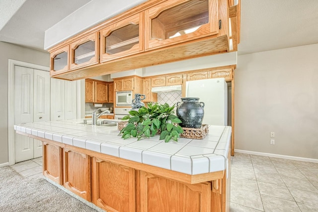 kitchen featuring light tile patterned floors, white appliances, a sink, decorative backsplash, and glass insert cabinets