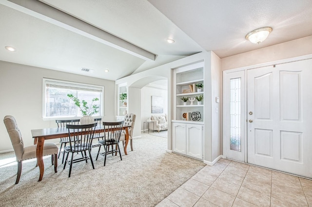 entryway featuring arched walkways, vaulted ceiling with beams, visible vents, light carpet, and light tile patterned flooring