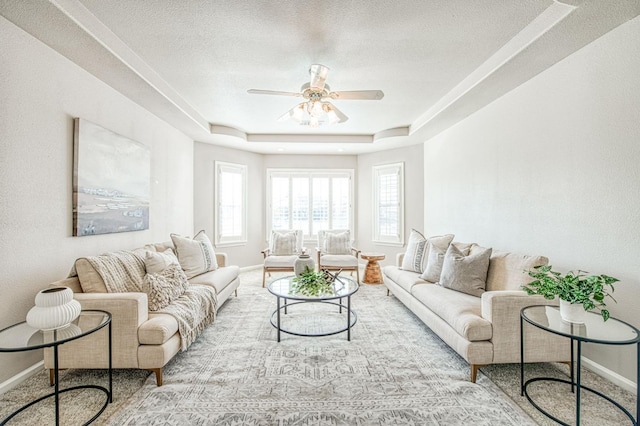 living room with baseboards, a tray ceiling, ceiling fan, and a textured ceiling