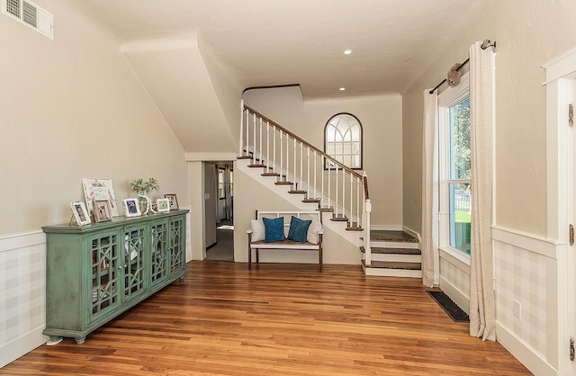 entrance foyer with wood finished floors, a wainscoted wall, visible vents, and stairs