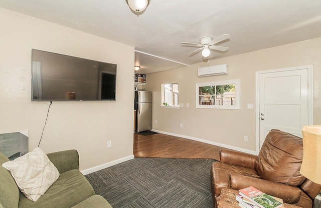 living room featuring a wall unit AC, ceiling fan, baseboards, and wood finished floors