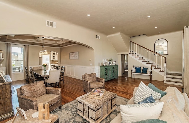 living room featuring arched walkways, stairway, wood finished floors, and visible vents