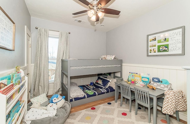 bedroom with wainscoting, wood finished floors, visible vents, and a ceiling fan