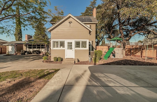 traditional-style house with a playground, a chimney, entry steps, roof mounted solar panels, and fence