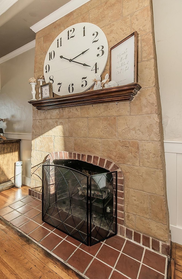 interior details with a large fireplace, ornamental molding, wood finished floors, and wainscoting