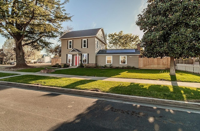 view of front of property featuring a front yard, fence, and roof mounted solar panels