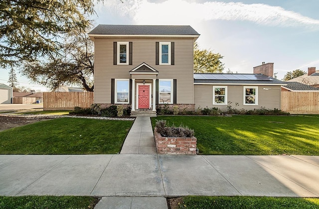 view of front of house with roof mounted solar panels, fence, and a front lawn