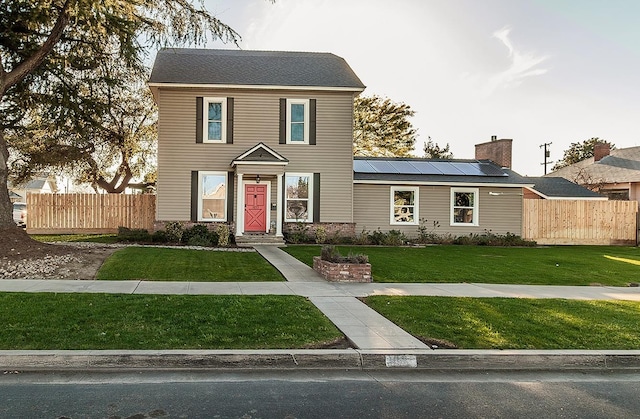 view of front of home featuring a front lawn, fence, and roof mounted solar panels