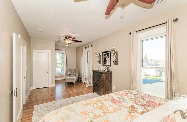 bedroom with a textured ceiling, a ceiling fan, visible vents, baseboards, and light wood-type flooring