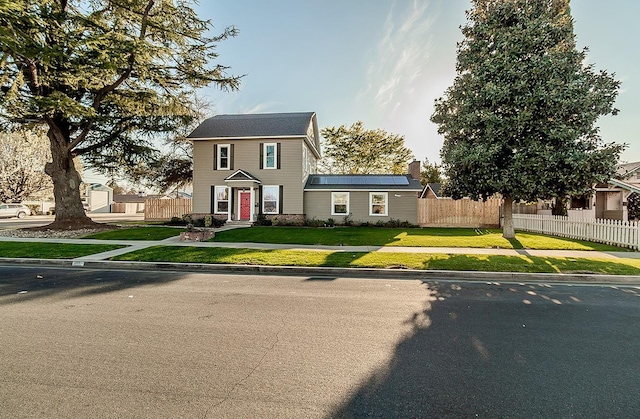 colonial home with a front yard, fence, and solar panels