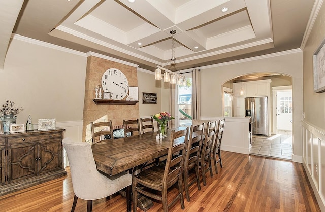 dining room featuring light wood finished floors, arched walkways, coffered ceiling, and wainscoting