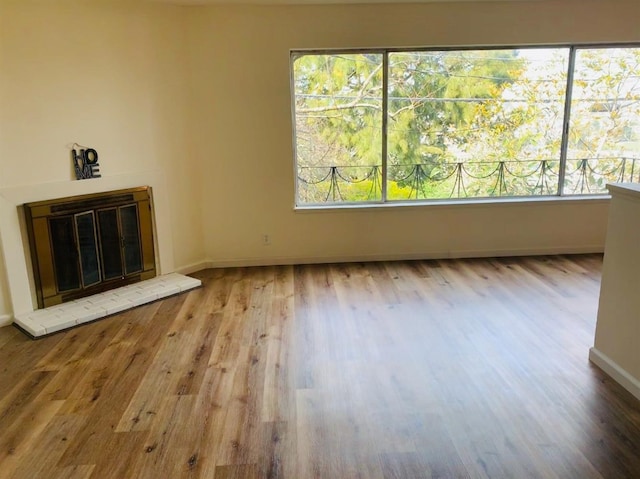 unfurnished living room featuring baseboards, wood finished floors, and a glass covered fireplace