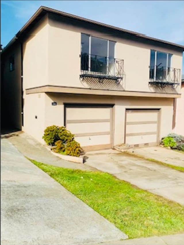 view of front of property with concrete driveway, an attached garage, a balcony, and stucco siding