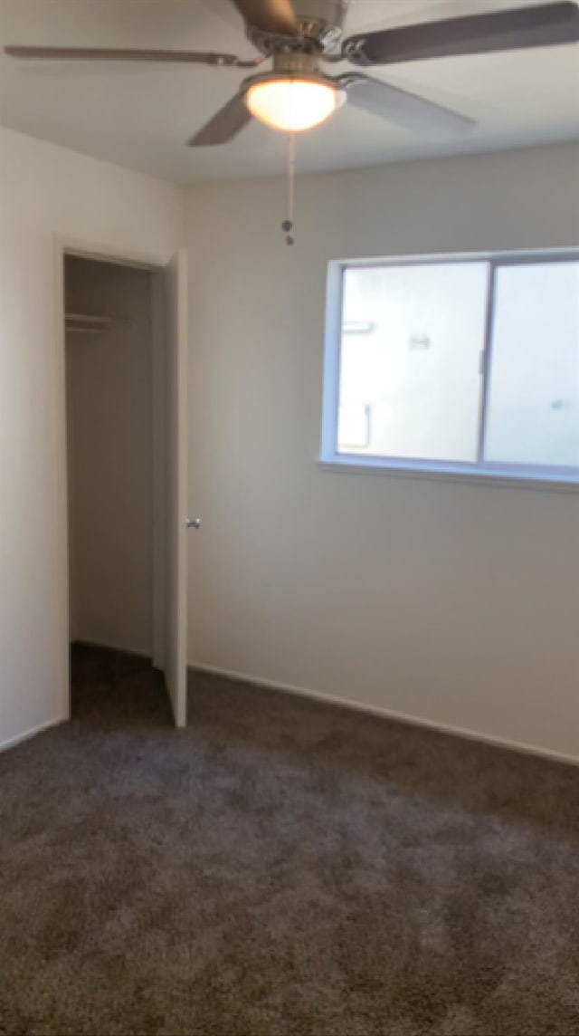 unfurnished bedroom with a ceiling fan, dark colored carpet, and a closet