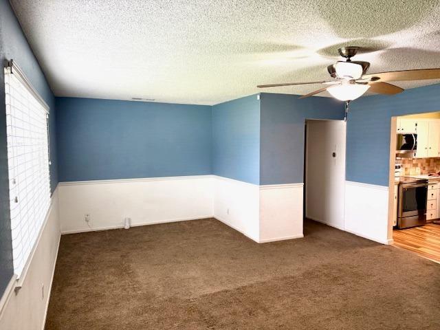 carpeted empty room featuring a ceiling fan, a wainscoted wall, and a textured ceiling