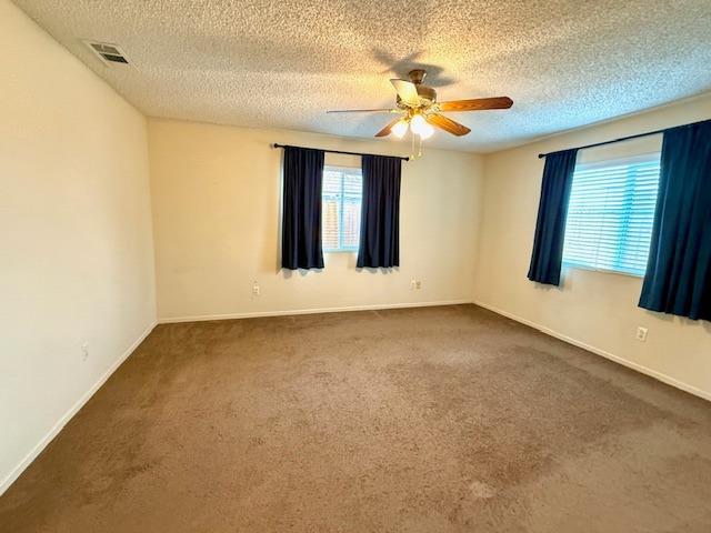 carpeted spare room featuring visible vents, a textured ceiling, a ceiling fan, and baseboards