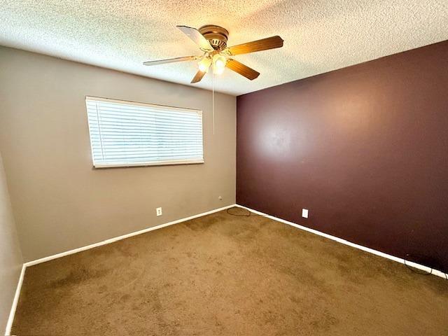 carpeted spare room with baseboards, a ceiling fan, and a textured ceiling