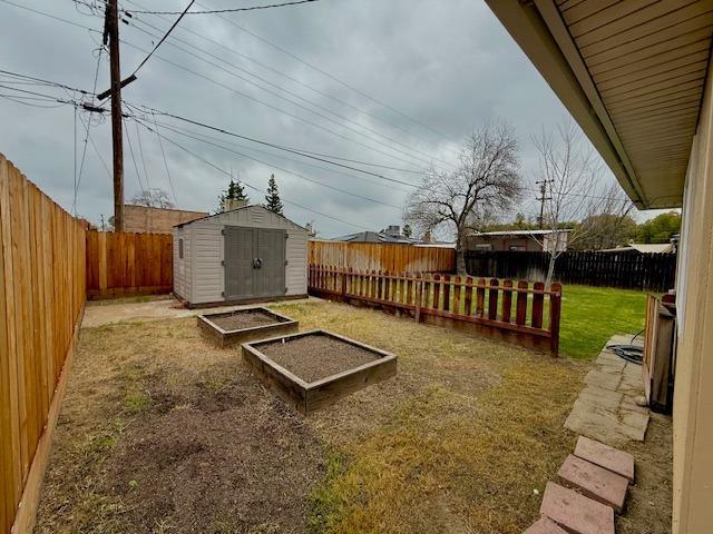 view of yard featuring a garden, an outdoor structure, a fenced backyard, and a storage shed