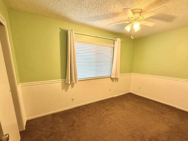 empty room featuring a ceiling fan, dark carpet, a textured ceiling, and baseboards