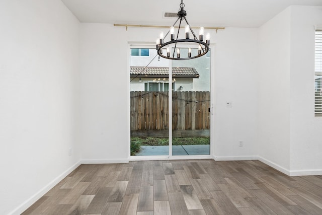 unfurnished dining area with a healthy amount of sunlight, baseboards, a chandelier, and wood finished floors