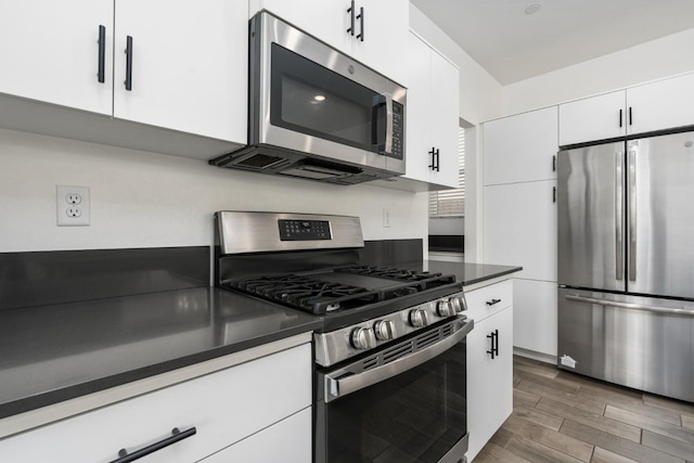 kitchen featuring dark countertops, white cabinetry, wood tiled floor, and appliances with stainless steel finishes