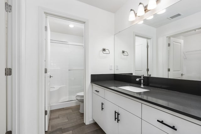 bathroom featuring toilet, wood finished floors, vanity, visible vents, and a stall shower