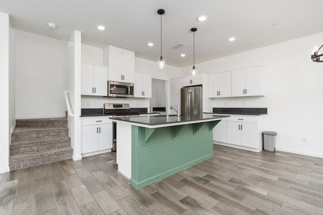 kitchen featuring dark countertops, wood tiled floor, appliances with stainless steel finishes, and a kitchen breakfast bar