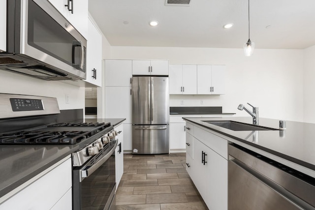 kitchen with stainless steel appliances, a sink, white cabinets, dark countertops, and pendant lighting