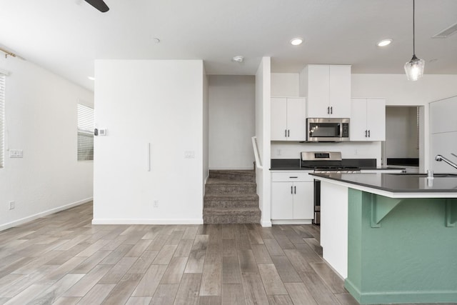 kitchen with stainless steel appliances, light wood finished floors, dark countertops, and a sink