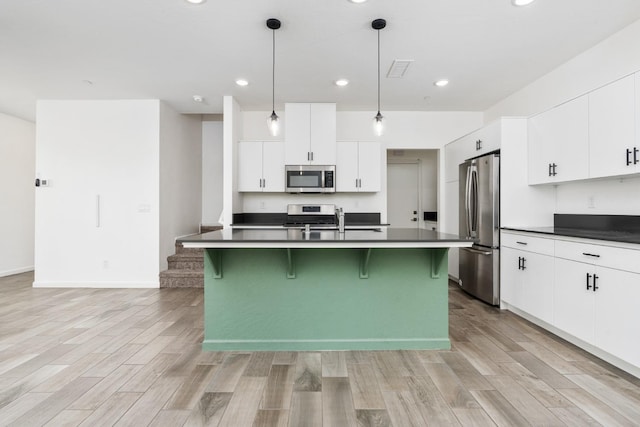 kitchen featuring a breakfast bar, a sink, appliances with stainless steel finishes, light wood-type flooring, and dark countertops