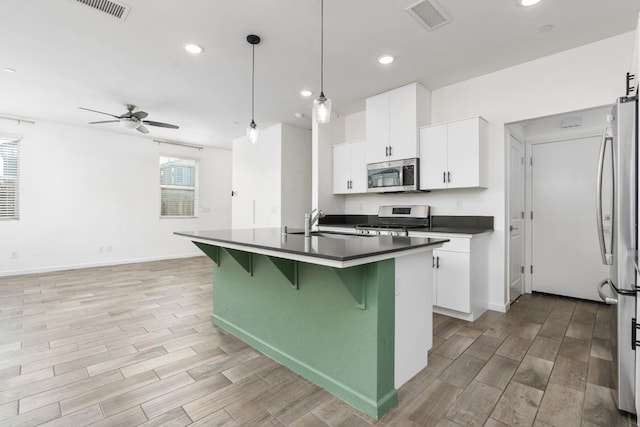 kitchen with a breakfast bar area, dark countertops, visible vents, appliances with stainless steel finishes, and a sink