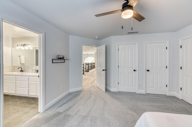 bedroom featuring two closets, visible vents, light carpet, a sink, and ensuite bath