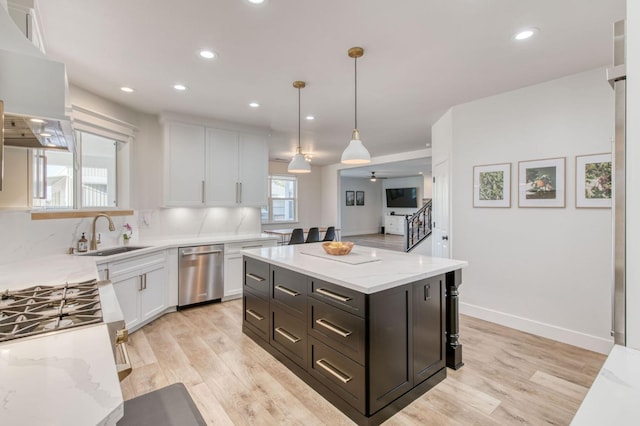 kitchen with light stone countertops, light wood-type flooring, stainless steel dishwasher, white cabinetry, and a sink