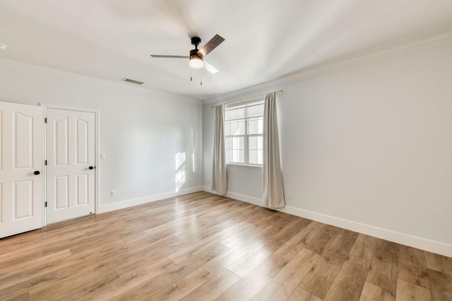 spare room featuring light wood finished floors, baseboards, visible vents, and crown molding