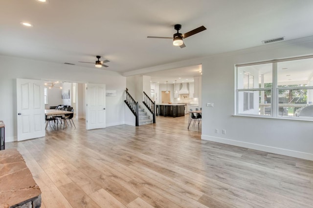 unfurnished living room featuring light wood-style floors, stairs, visible vents, and crown molding