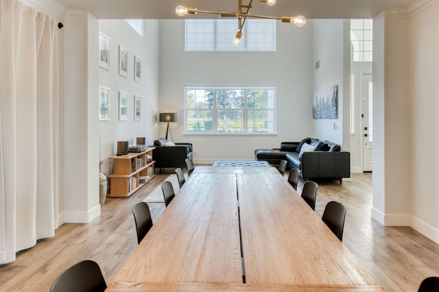 dining room featuring a towering ceiling, baseboards, a chandelier, and wood finished floors