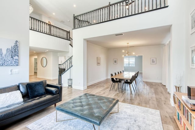 living room featuring light wood-style flooring, visible vents, a towering ceiling, baseboards, and ornamental molding