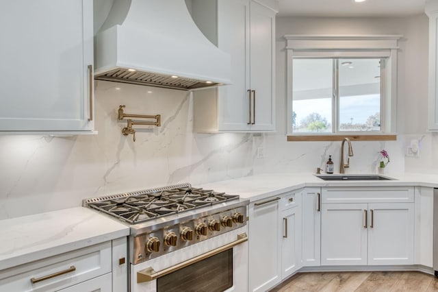 kitchen with premium range hood, a sink, high end range, and white cabinetry