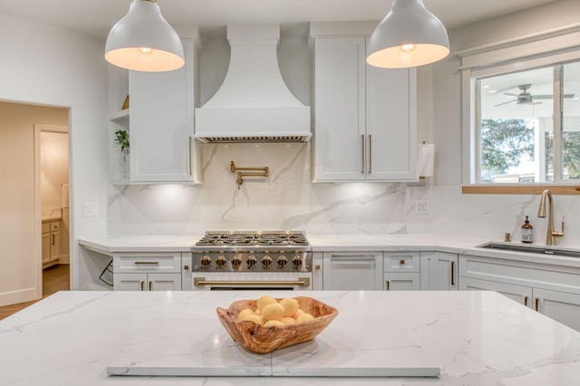 kitchen featuring light stone counters, stainless steel stove, a sink, backsplash, and custom exhaust hood