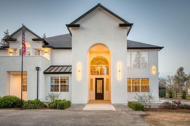 view of front of home featuring metal roof, a balcony, a shingled roof, stucco siding, and a standing seam roof