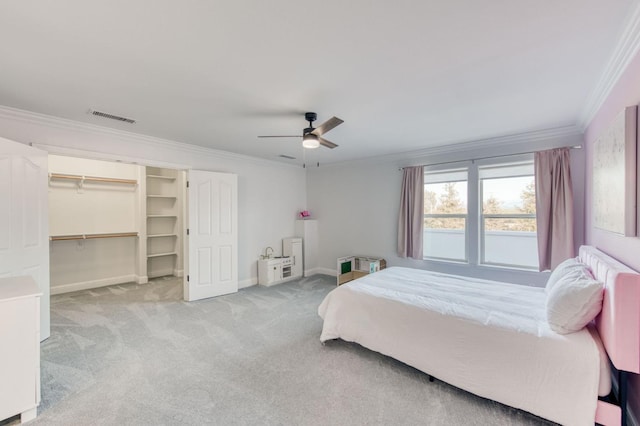 carpeted bedroom with a ceiling fan, visible vents, baseboards, a spacious closet, and ornamental molding