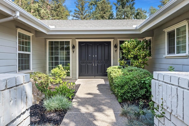 view of exterior entry with covered porch and roof with shingles