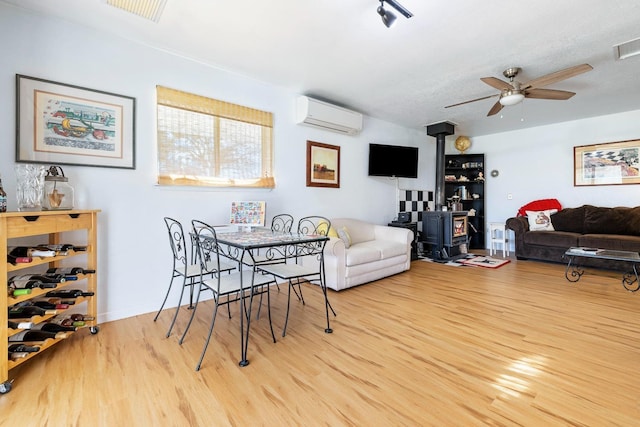 dining room with a wood stove, a wall unit AC, ceiling fan, and wood finished floors