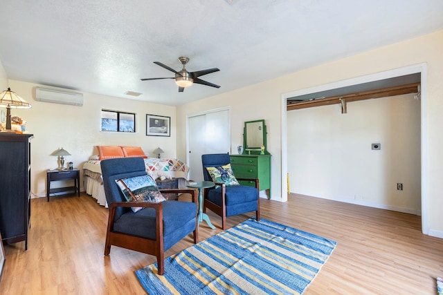 bedroom featuring ceiling fan, a wall unit AC, visible vents, baseboards, and light wood-style floors