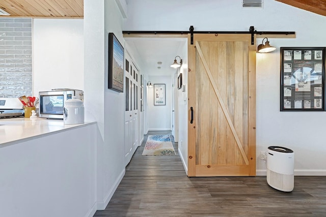 corridor featuring dark wood-style flooring, visible vents, baseboards, and a barn door